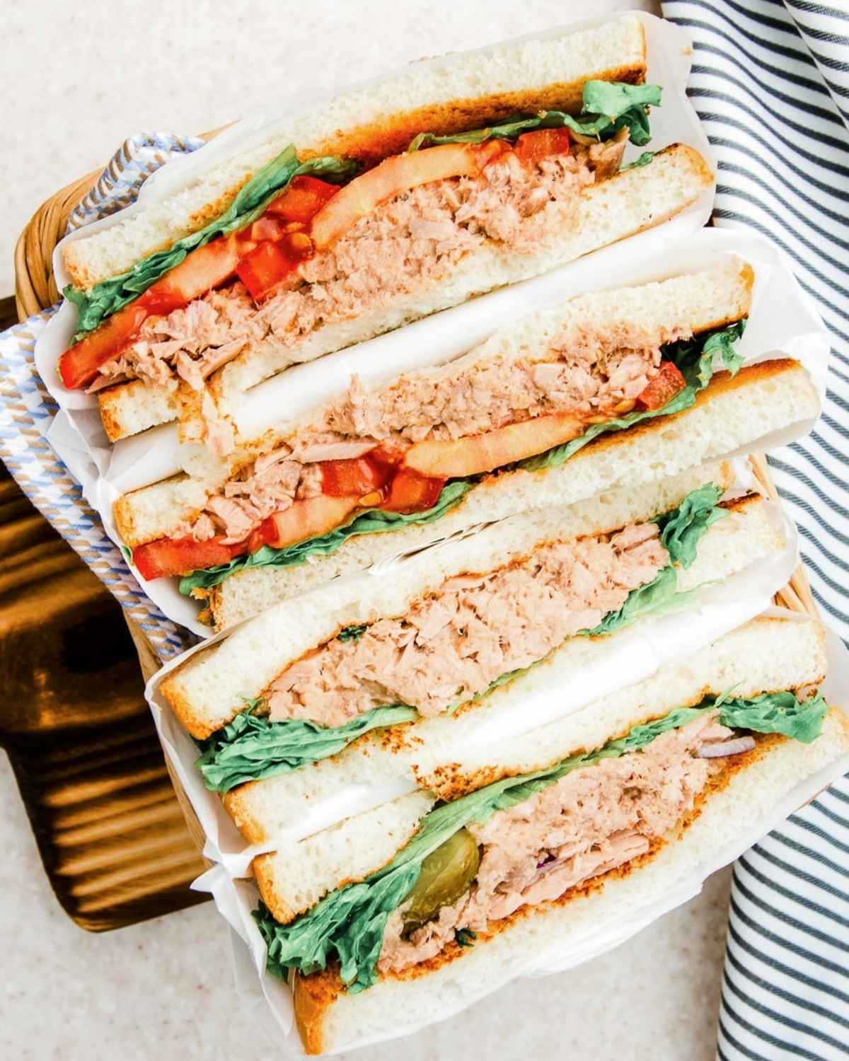two triple decker sandwich filled with salmon salad, tomato and greens over a wooden board