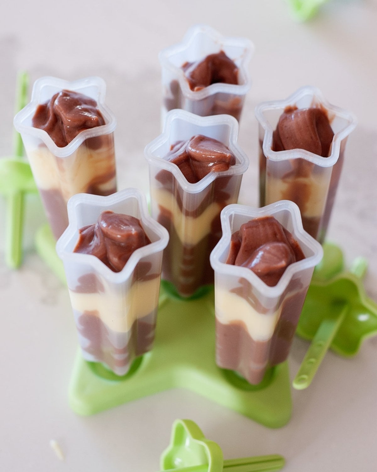 six popsicle molds filled with banana and chocolate pudding