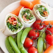 three salmon pinwheels surronded by cherry tomatoes, baby carrots and snap peas