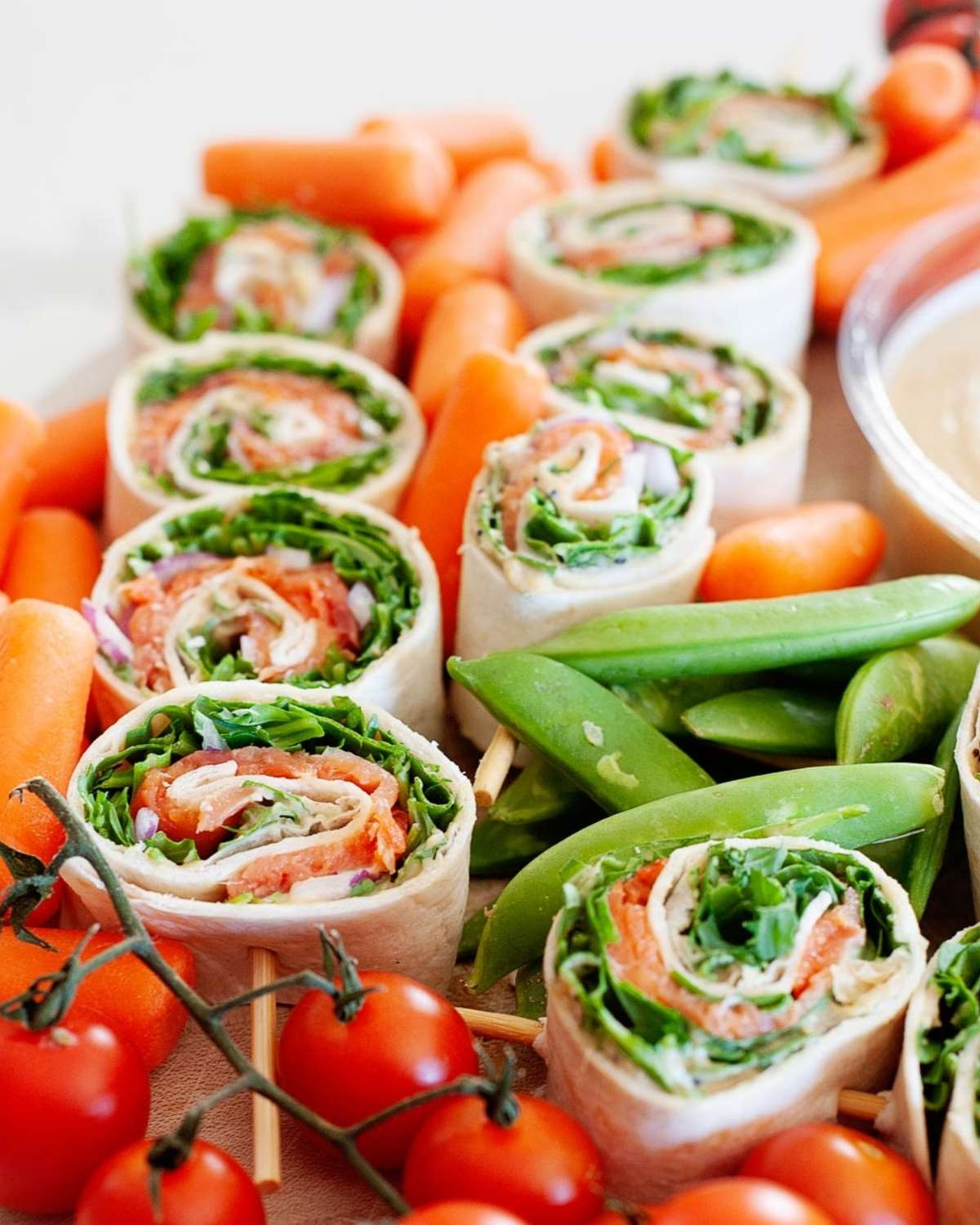nine salmon pinwheels surrondead by cherry tomatoes, baby carrots and snap peas