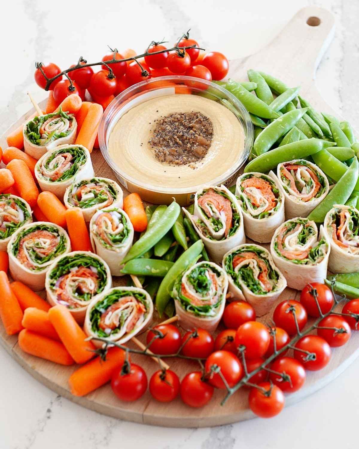 salmon pinwheels on a platter with hummus, cherry tomatoes, baby carrots and snap peas