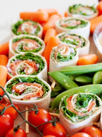 nine salmon pinwheels surrondead by cherry tomatoes, baby carrots and snap peas