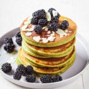 fluffy stack of green avocado pancakes topped with berries and slivered almonds on a plate
