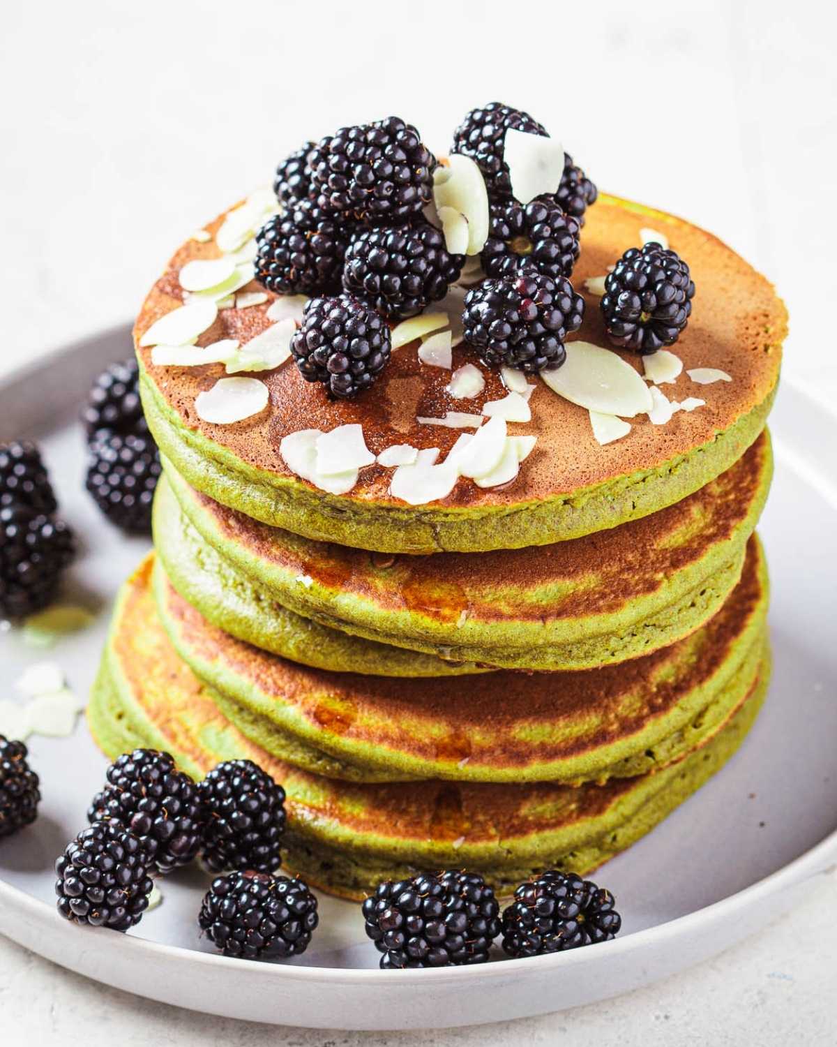 fluffy stack of green avocado pancakes topped with berries and slivered almonds on a plate