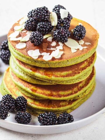 fluffy stack of green avocado pancakes topped with berries and slivered almonds on a plate