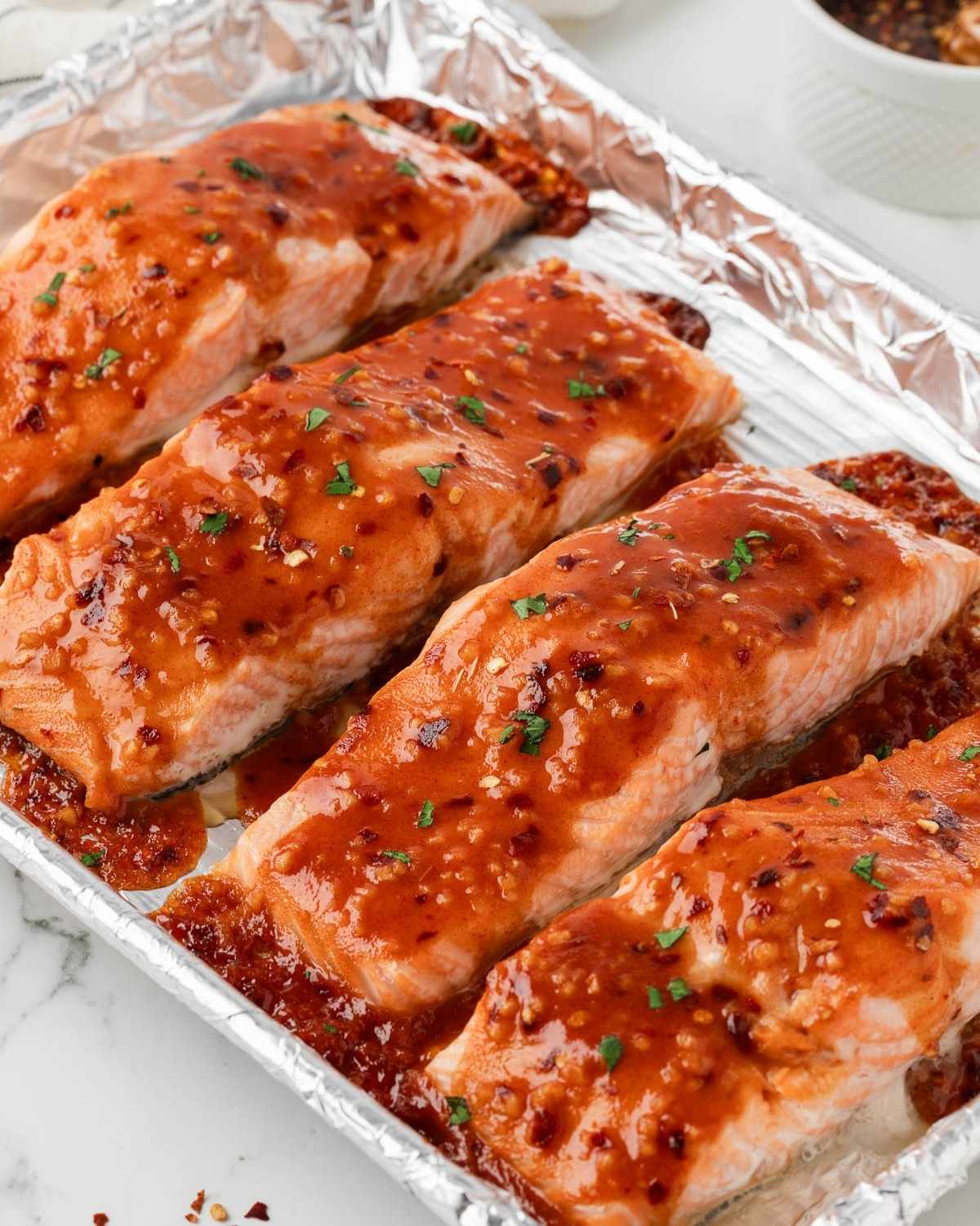 four salmon fillets on a baking sheet covered with hot honey sauce