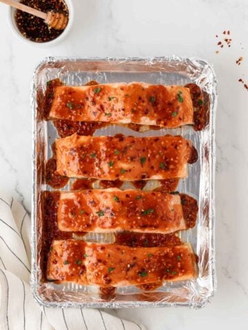 four salmon fillets on a baking sheet covered with hot honey sauce