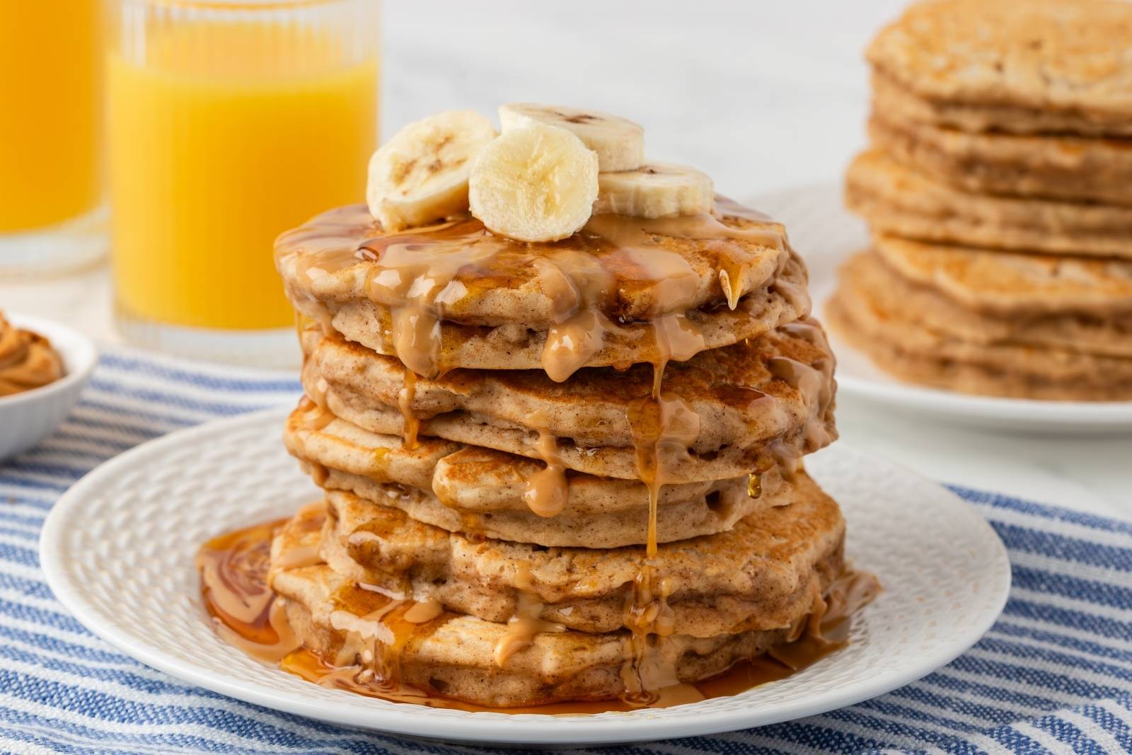 fluffy stack of peanut butter banana pancakes on a plate topped with banana slices, peanut butter drizzle and some syrup