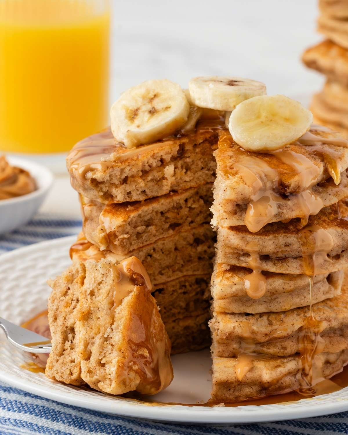 peanut butter banana pancakes on a plate, sliced to show their fluffy texture, topped with banana slices, peanut butter drizzle and some syrup