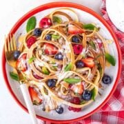 overhead view of pancake batter cooked to look like spaghetti strands on a plate, with fresh fruit and powdered sugar on top as toppings