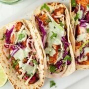 three fish tacos with cilantro sauce and slaw on a white tray