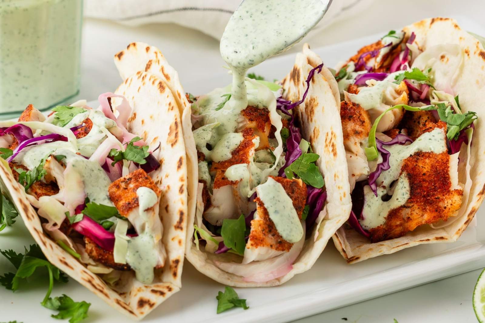 three fish tacos with cilantro sauce and slaw on a white tray