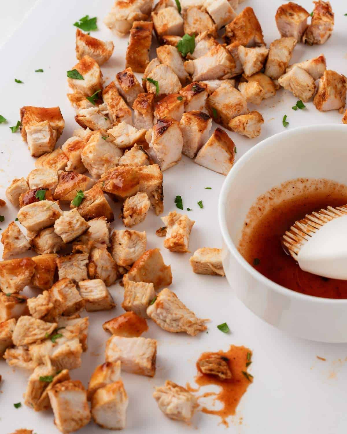 chopped buffalo chicken breasts on a board with extra buffalo sauce in a dish