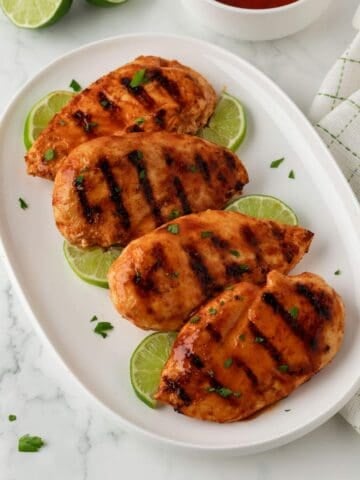 overhead view of grilled Buffalo chicken breasts on a plate with lime wedges