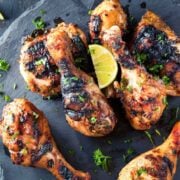 grilled chicken drumsticks garnished with parsley and a lime wedge, served on a dark stone platter.