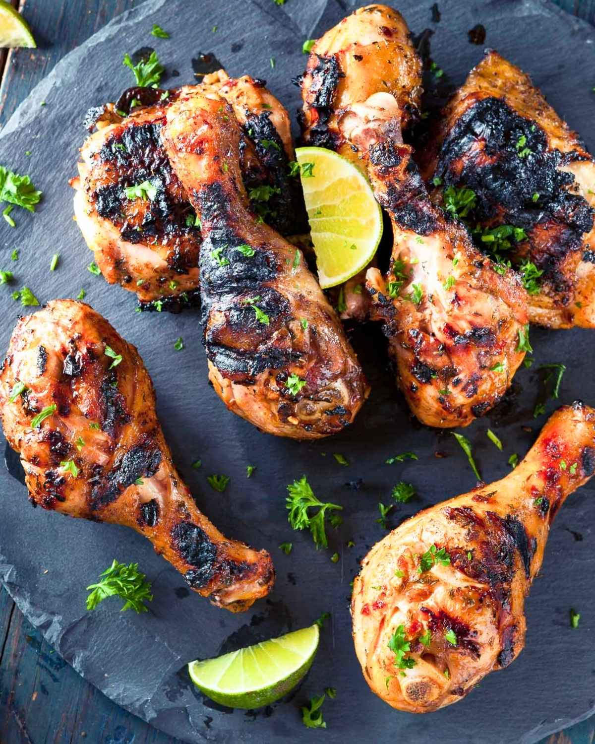 grilled chicken drumsticks garnished with parsley and a lime wedge, served on a dark stone platter.