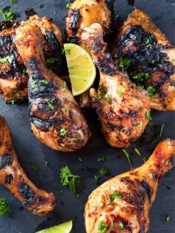 grilled chicken drumsticks garnished with parsley and a lime wedge, served on a dark stone platter.
