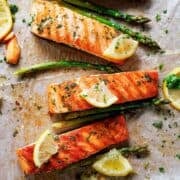 three salmon fillets with lemon wedges and a few asparagus on the side