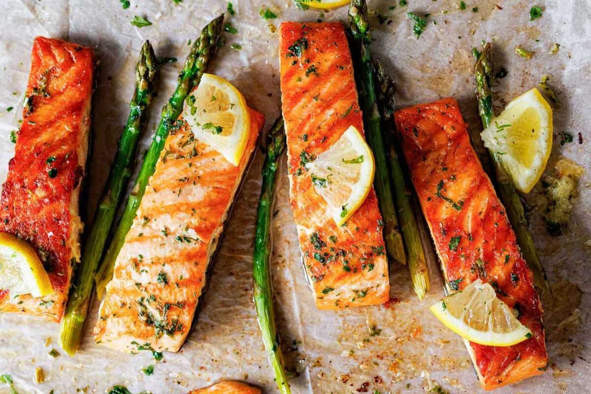 four salmon fillets with lemon wedges and a few asparagus on the side