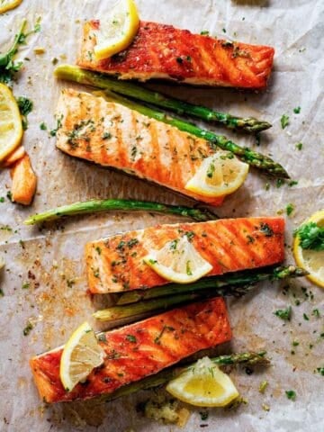 four salmon fillets with lemon wedges and a few asparagus on the side
