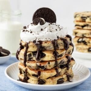 stack of oreo pancakes on a plate topped with chocolate syrup, whipped cream, and oreos on top