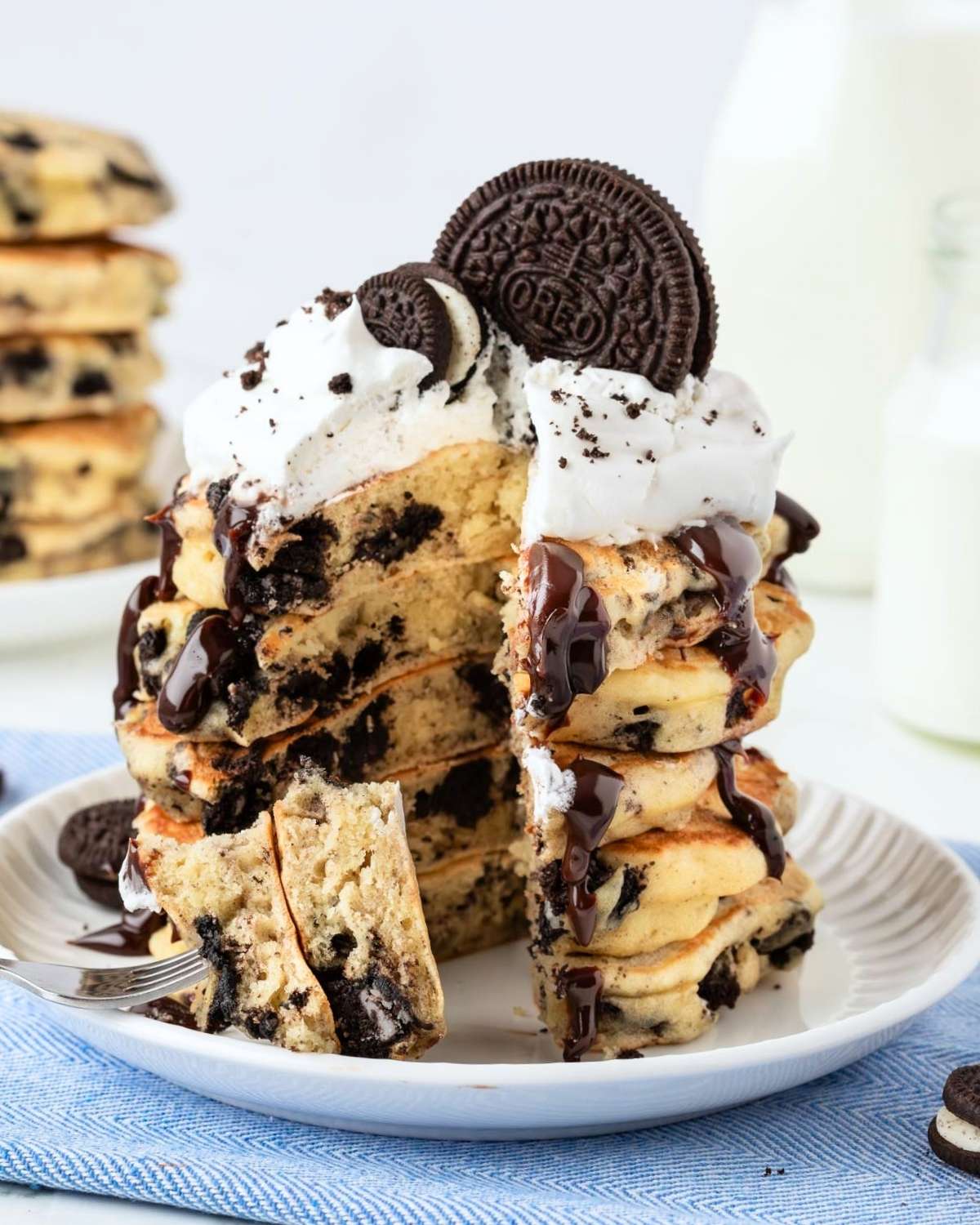 stack of oreo pancakes on a plate topped with chocolate syrup, whipped cream, and oreos on top