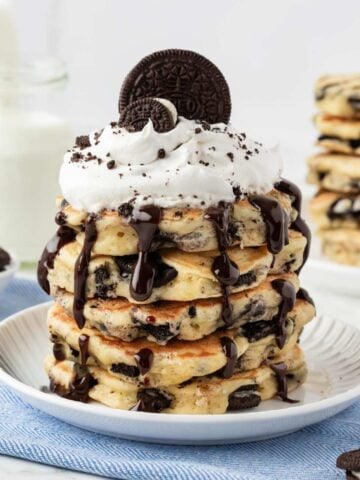 stack of oreo pancakes on a plate topped with chocolate syrup, whipped cream, and oreos on top