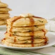 stack of fluffy zucchini pancakes on a plate topped with butter and pancake syrup