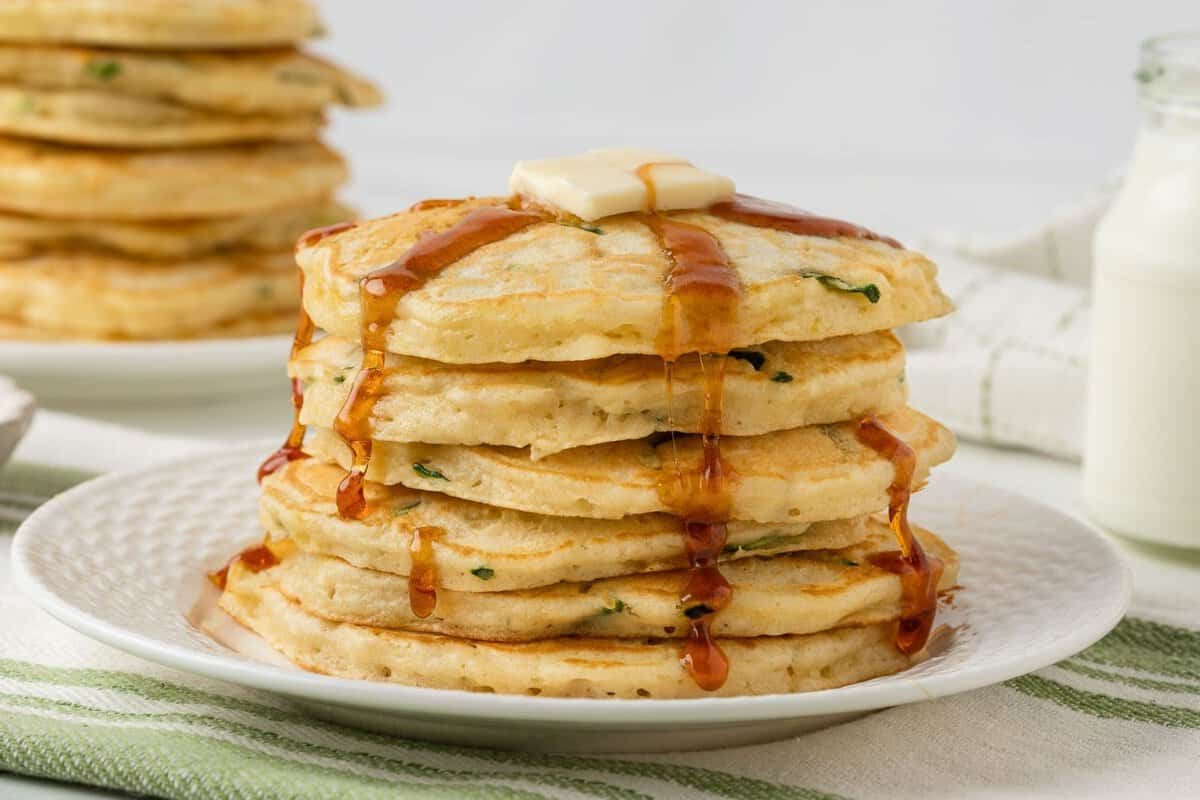 stack of fluffy zucchini pancakes on a plate topped with butter and pancake syrup