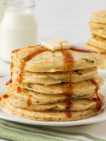 stack of fluffy zucchini pancakes on a plate topped with butter and pancake syrup