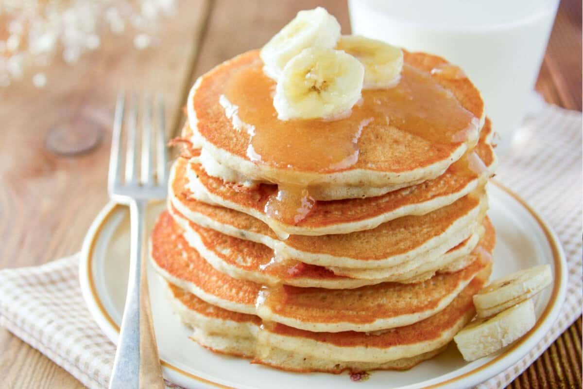 a stack of applesauce pancakes topped with syrup and banana slices