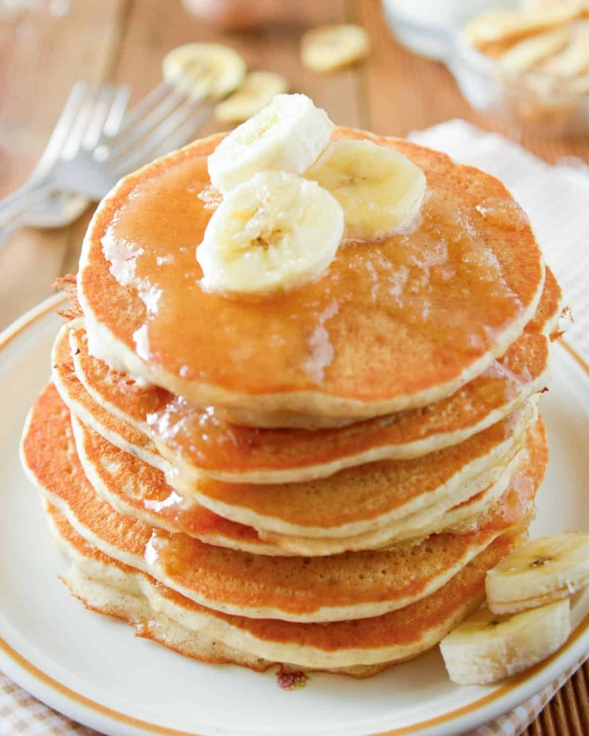 a stack of applesauce pancakes topped with syrup and banana slices