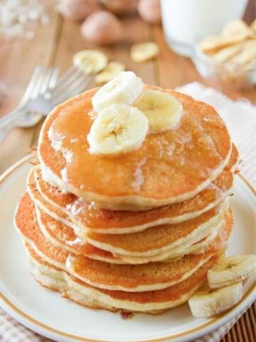 a stack of applesauce pancakes topped with syrup and banana slices
