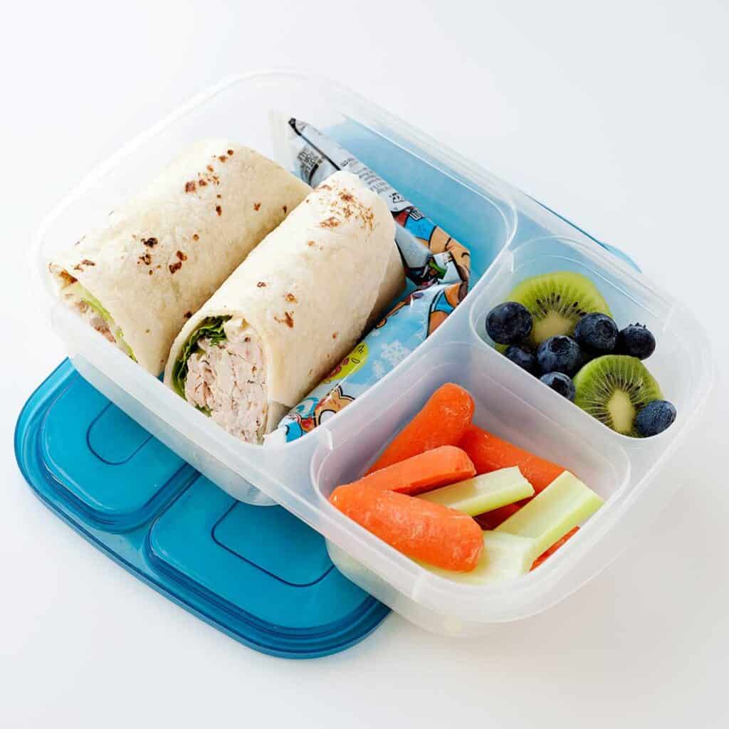 chicken ranch wrap sliced in halves in a lunchbox with veggies and fruit