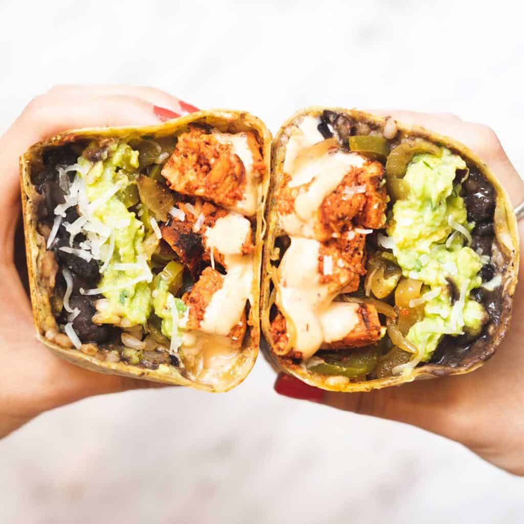 hands holding two halves of a chipotle chicken wrap