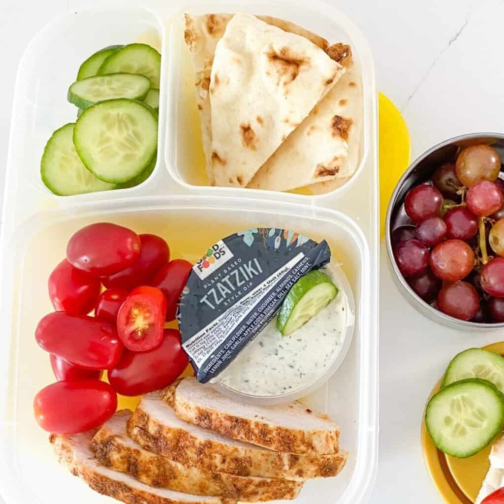 bento box with chicken, tzatziki sauce, pita chicps and veggies