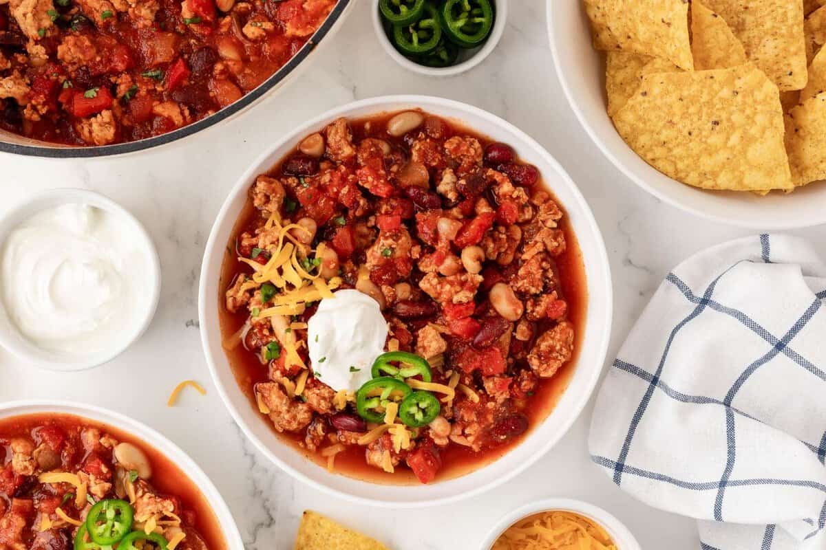 overhead view of a bowl of chicken chili with toppings served with chips on the side, sour cream and cheese.