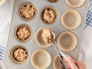overhead view scooping banana oatmeal muffin batter into a lined muffin pan