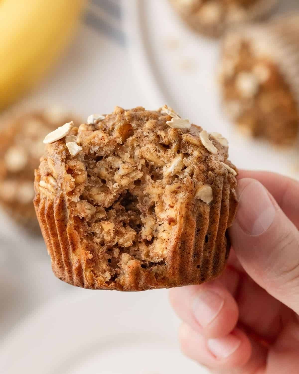 a hand holding up a muffin to provide a close up view of the texture inside a baked healthy banana oatmeal muffins