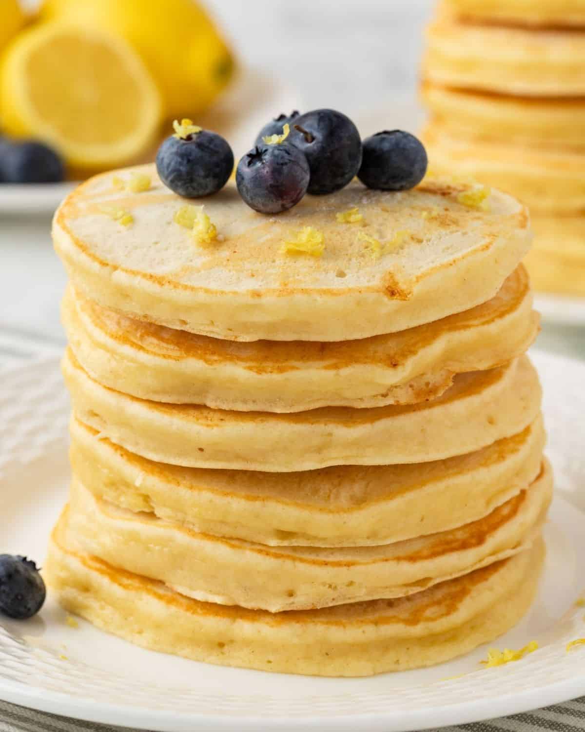 fluffy stack of lemon pancakes on a plate, topped with blueberries and lemon zest.