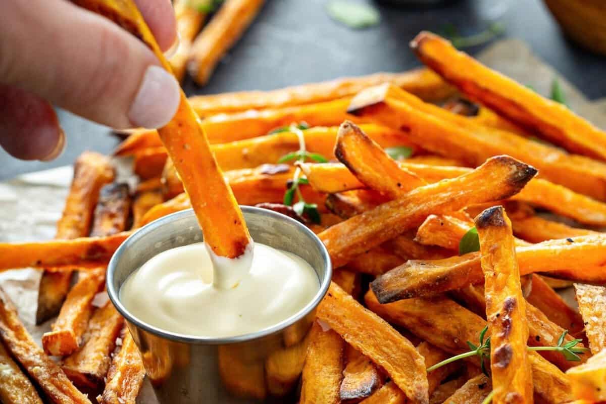 front view of sweet potatoes cooked in the air fryer being dipped in mayo