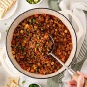 overhead view of a dutch oven with chili with vegetables using a ladle to serve