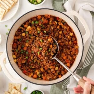 overhead view of a dutch oven with chili with vegetables using a ladle to serve