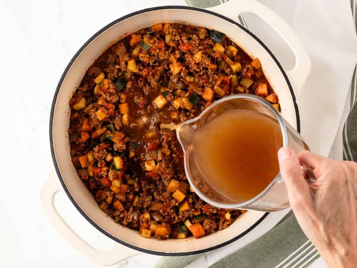 overhead view of cooked chili with vegetables adding broth to thin it out