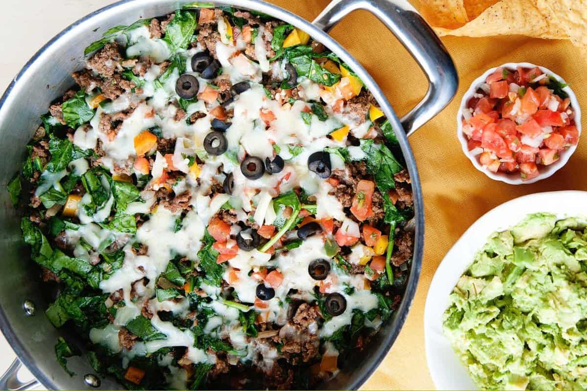 overhead view of a ground beef and spinach skillet meal with cheese on top and a side of guac