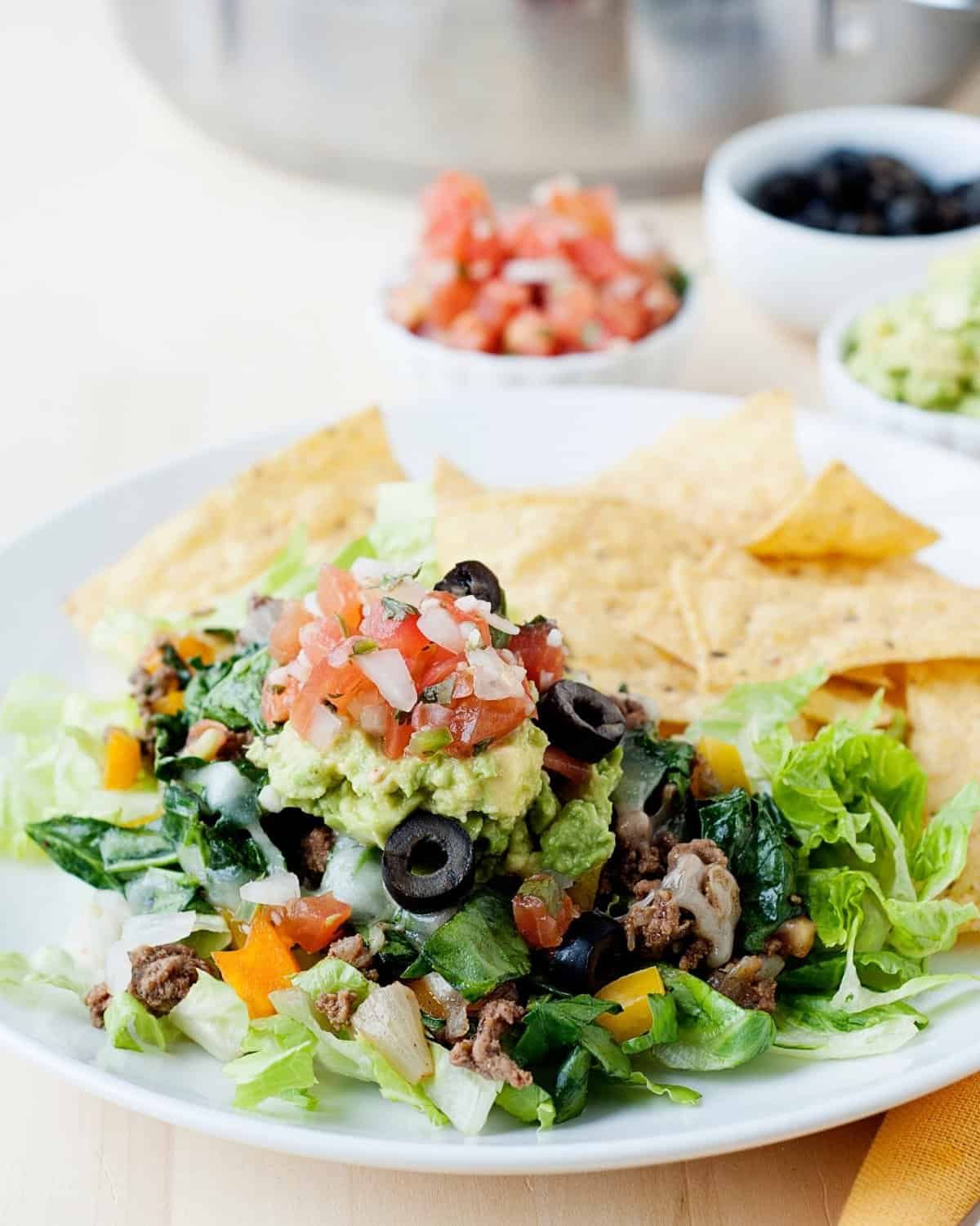 a plate with a ground beef and spinach skillet meal topped with guacamole and pico de gallo and served with chips