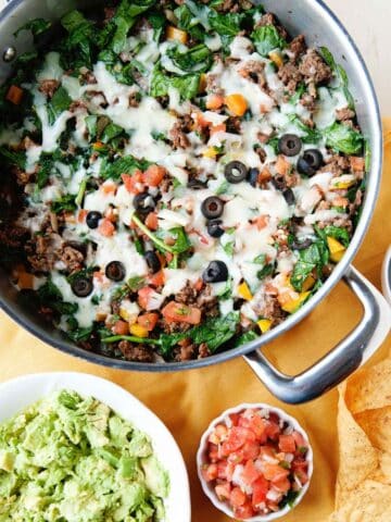 overhead view of a ground beef and spinach skillet meal with cheese melted on top and a side of guac and pico