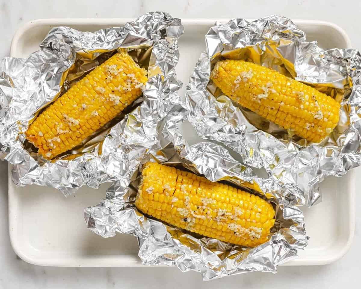 overhead view of 3 pieces of corn on the cob on top of foil topped with a garlic butter sauce.