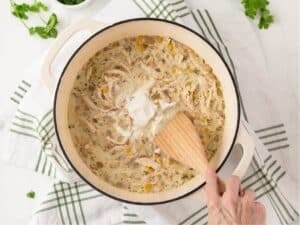 a hand stirring white chicken chili in a pot with a wooden spoon