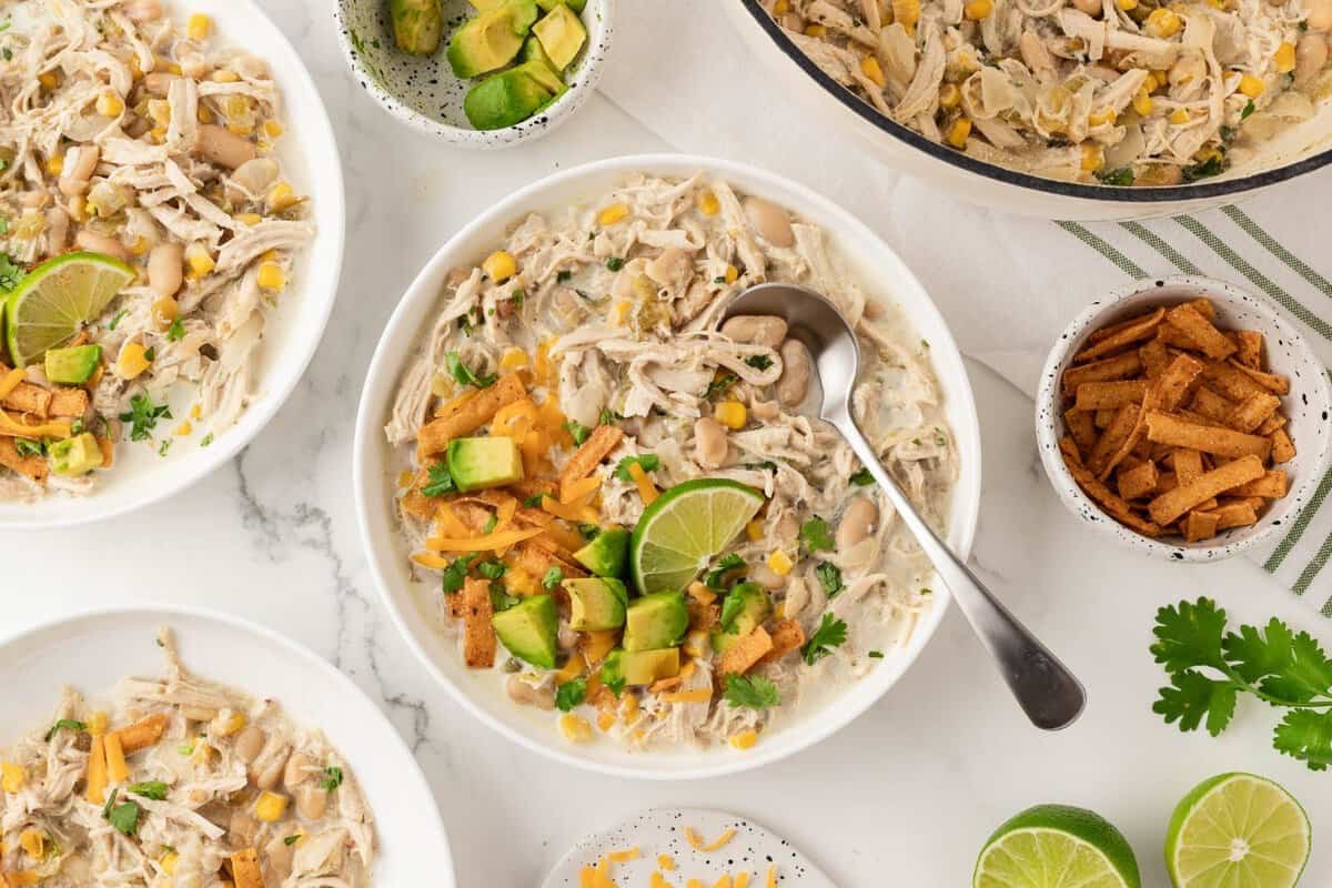 overhead view of three bowls with white rotisserie chicken chili, surrounded by limes wedges and toppings